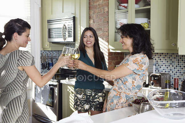 Trois amies levant un verre de vin blanc dans la cuisine — Photo de stock