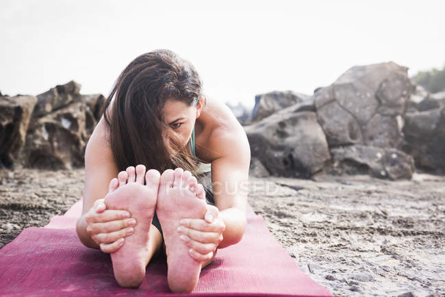 Mujer sosteniendo sus pies practicando yoga en la playa - foto de stock