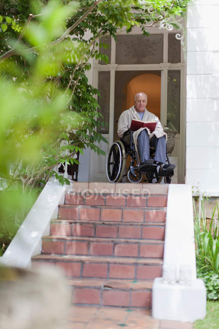 Older man reading in wheelchair on the porch — Stock Photo