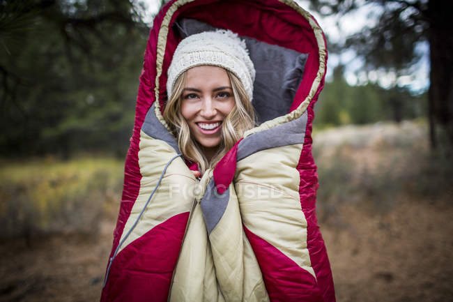Portrait of young woman wearing knit hat wrapped in sleeping bag, Lake Tahoe, Nevada, USA — Stock Photo