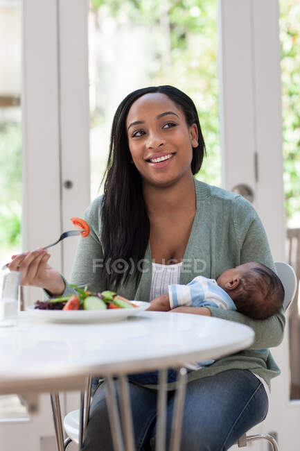 Madre sosteniendo al bebé hijo y almorzando - foto de stock