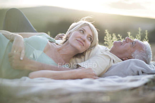 Зрелая пара, лежащая вместе на одеяле на открытом воздухе — стоковое фото