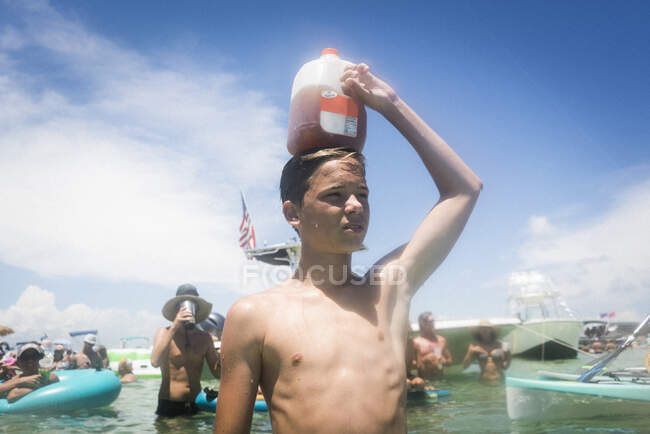 Teenage boy in water holding juice carton on head, Crab Island, Emerald Coast, Gulf of Mexico, USA — Stock Photo