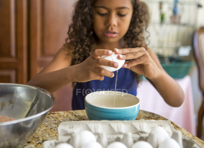 Chica rompiendo huevos en un tazón mirando hacia abajo - foto de stock