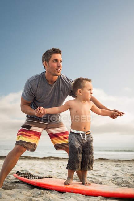 Young man teaching son to surf on beach — Stock Photo
