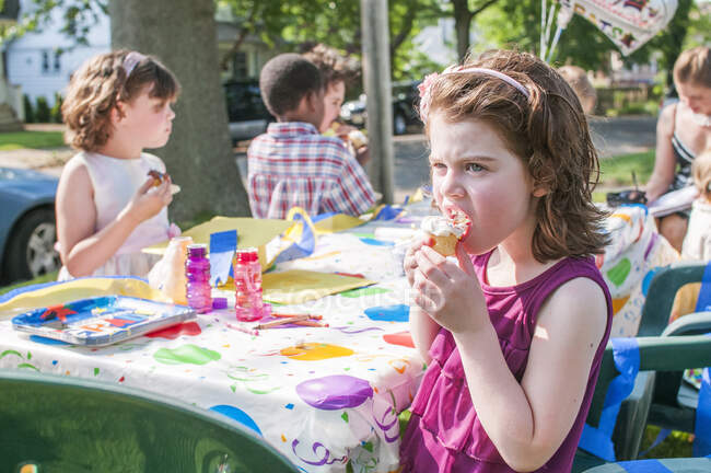 Молодая девушка ест мороженое на вечеринке детского сада — стоковое фото