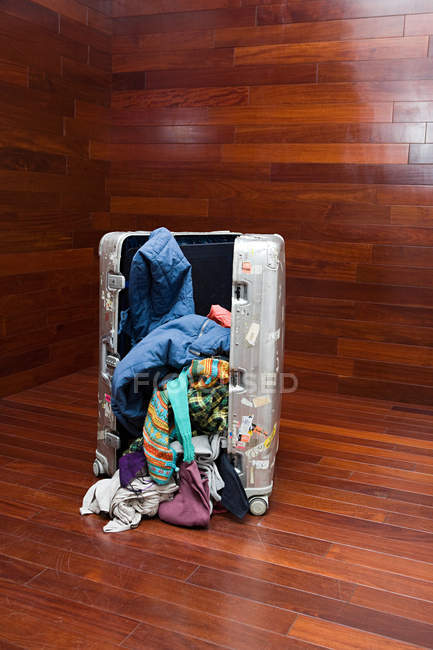 Valigia aperta con vestiti rovesciati sulla superficie di legno — Foto stock