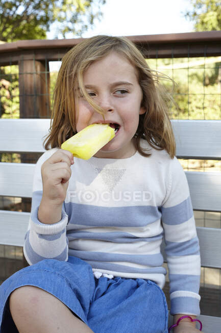 Porträt eines Mädchens, das eisgekühlten Lolli auf Gartenbank isst — Stockfoto