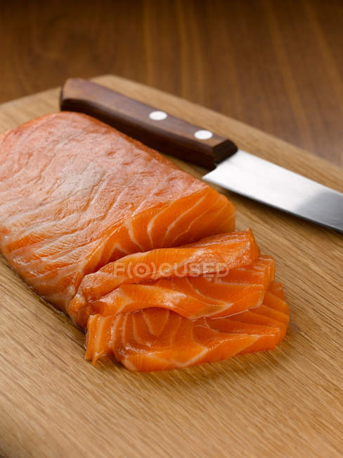 Salmón en rodajas y cuchillo en tabla de cortar - foto de stock