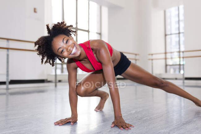 Молода жінка в танцювальній студії відпочиває на руках, нога простягається, дивлячись на камеру посміхаючись — стокове фото