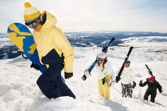 Snowboarders and skiers carrying equipment to the top of mountain — Stock Photo