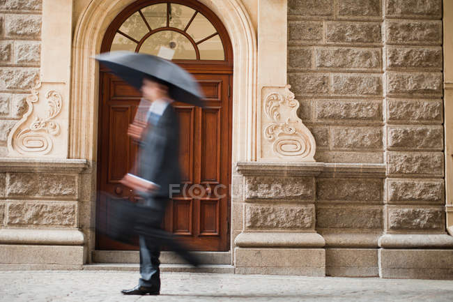 Vue latérale de l'homme d'affaires portant un parapluie sur la rue — Photo de stock