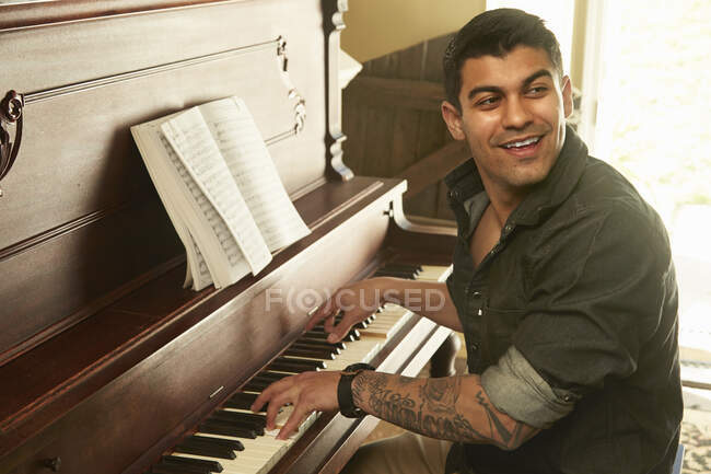 Jeune homme regardant par-dessus son épaule tout en jouant du piano — Photo de stock