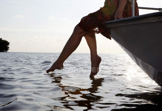 Старшая женщина сидит на краю моторной лодки с ногами в воде — стоковое фото