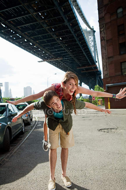 Young man carrying woman under bridge — Stock Photo