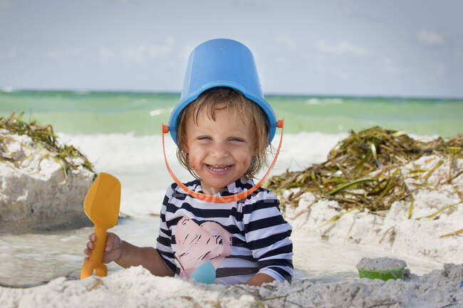 Baby girl with bucket over head on beach, Anna Maria Island, Florida, USA — Stock Photo