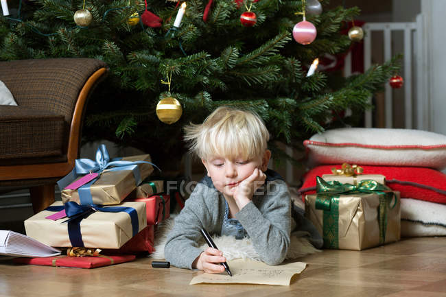 Menino escrevendo debaixo da árvore de Natal — Fotografia de Stock