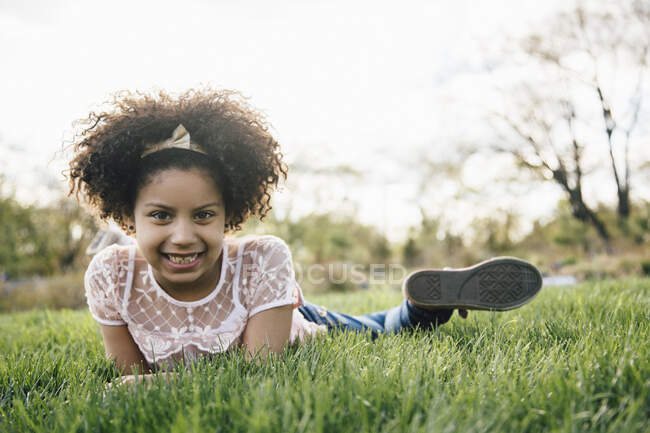 Visão de nível de superfície da menina deitada na frente na grama sorrindo, olhando para a câmera — Fotografia de Stock