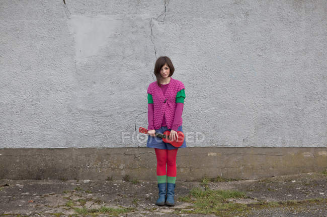 Giovane donna in piedi con ukulele contro il muro — Foto stock