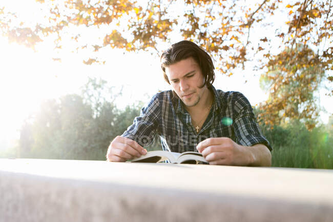 Giovane uomo all'aperto seduto a tavola guardando giù libro di lettura — Foto stock