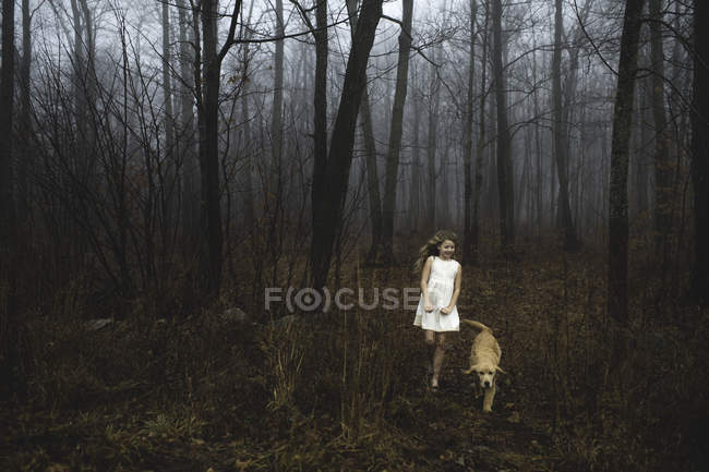 Дівчина в білій сукні, що гуляє з собакою в лісі — стокове фото