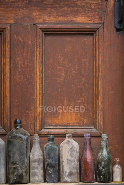 Vecchie bottiglie di vetro in fila accanto alla porta di legno — Foto stock