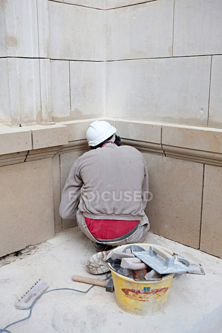 Vista trasera del trabajador de la construcción sentado delante de la pared y haciendo reparación - foto de stock