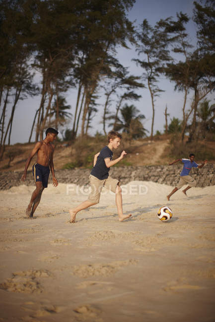 Chicos jugando fútbol en la playa de arena - foto de stock