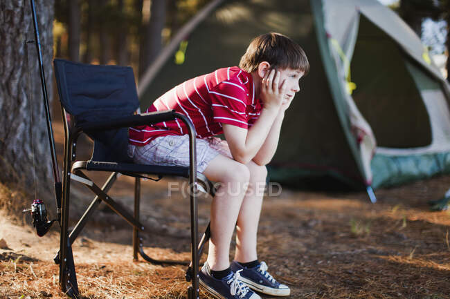 Niño aburrido en silla de césped en el camping - foto de stock