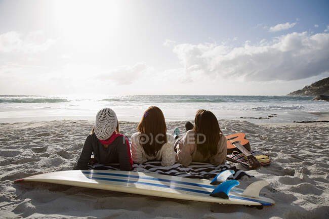 Три дівчини лежать на пляжі з дошкою для серфінгу — стокове фото