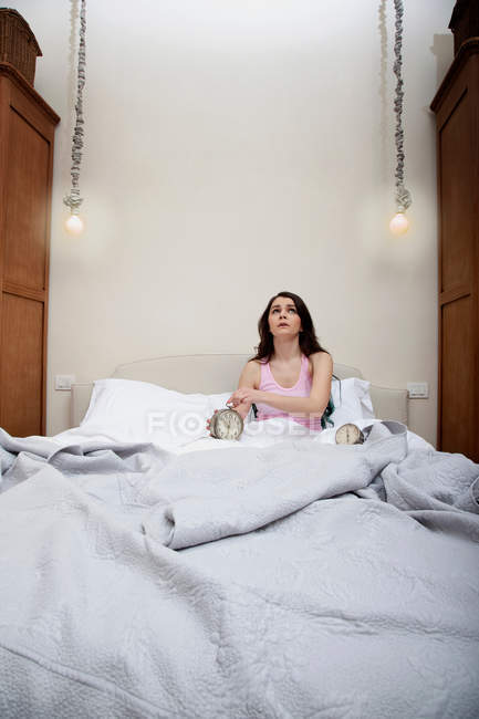 Жінка в ліжку тримає будильник — стокове фото