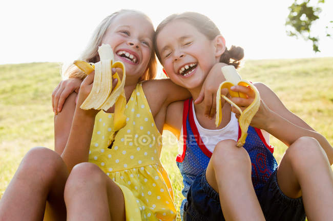Riant filles manger des bananes à l'extérieur — Photo de stock