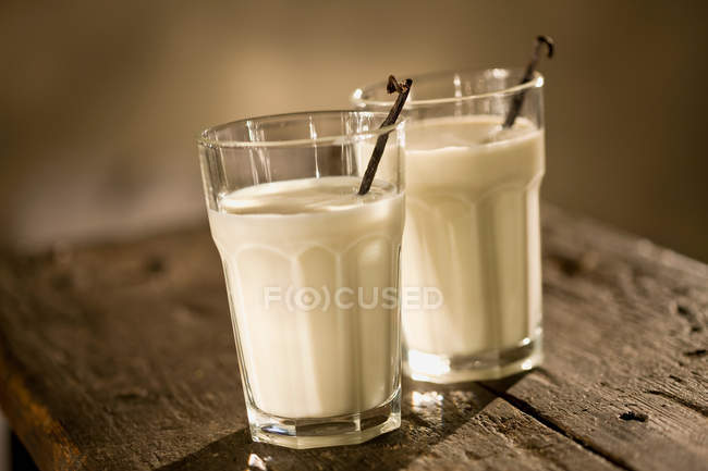 Latte e baccelli di vaniglia in bicchieri — Foto stock