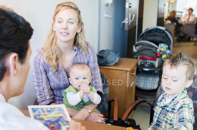 Madre sentada con dos hijos, conversando con el médico - foto de stock