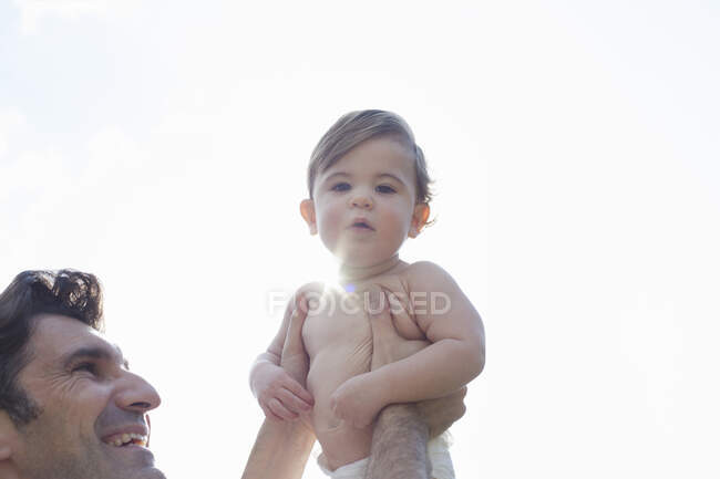 Low angle view of father holding up son, looking at camera — Stock Photo