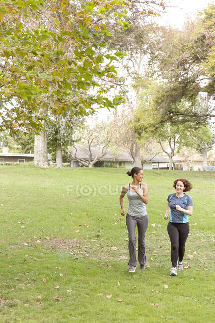 Vista frontal de longitud completa de las mujeres que usan ropa deportiva corriendo sobre hierba - foto de stock