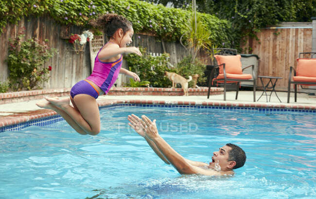 Seitenansicht des Vaters, der Mädchen beim Sprung in einen Swimmingpool erwischt, mitten in der Luft — Stockfoto