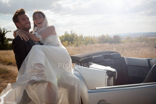 Newlywed groom carrying bride outdoors — Stock Photo