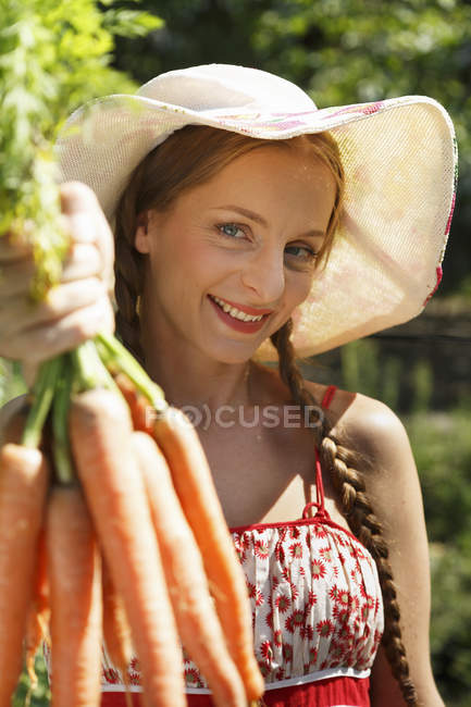 Porträt einer erwachsenen Frau im Garten, die ein Bündel Möhren in der Hand hält — Stockfoto