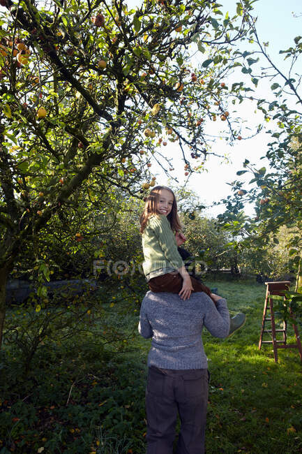 Girl on mother's shoulders in orchard — Stock Photo
