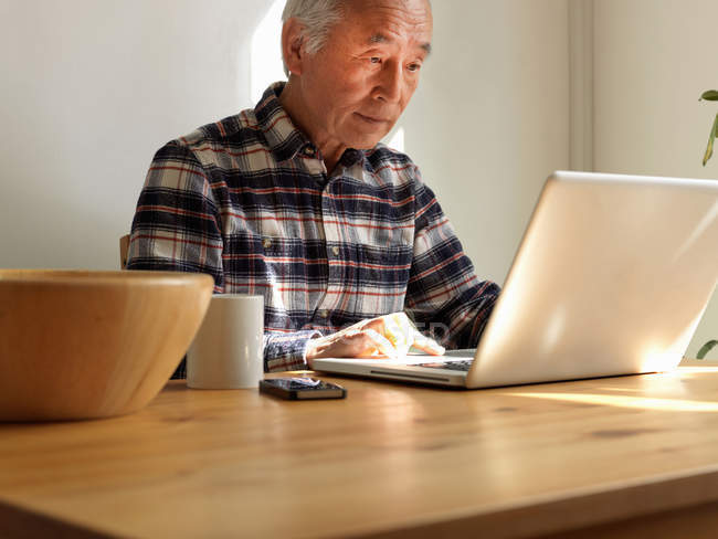 Uomo più anziano che utilizza il computer portatile a tavola — Foto stock