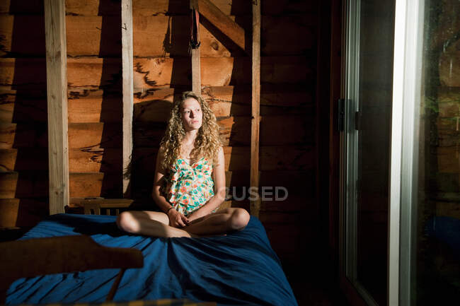 Дівчина-підліток виглядає сумно, сидячи на ліжку — стокове фото