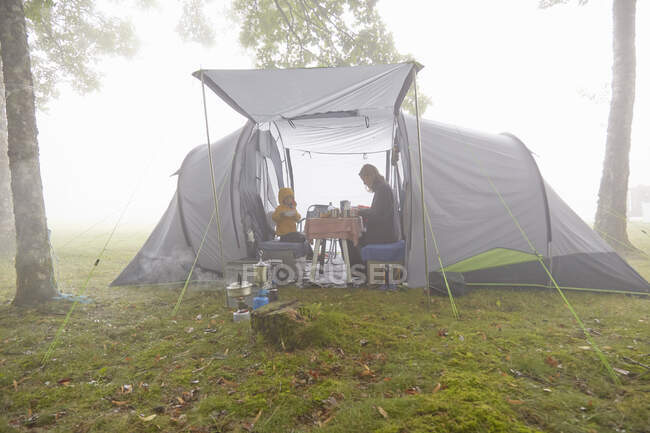 Mutter und Söhne frühstücken im Zelt in nebliger Landschaft — Stockfoto