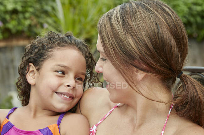 Cabeza y hombros de madre e hija usando trajes de baño cara a cara sonriendo - foto de stock