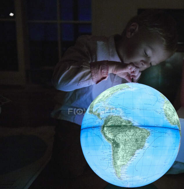 Young boy looking at illuminated globe in dark room — Stock Photo