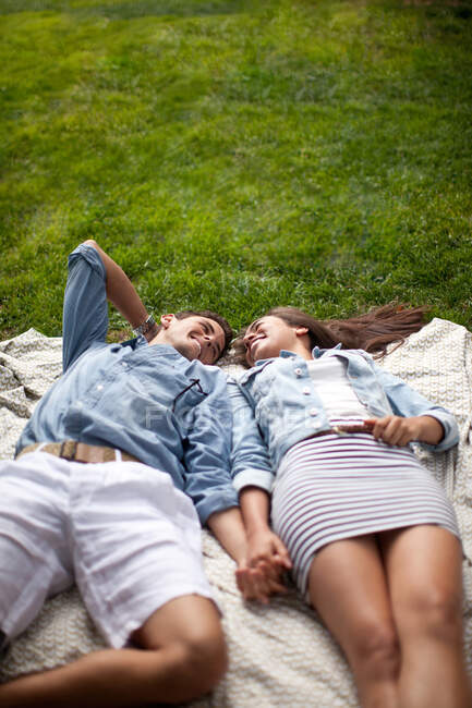 Jeune couple couché dans le parc et tenant la main — Photo de stock
