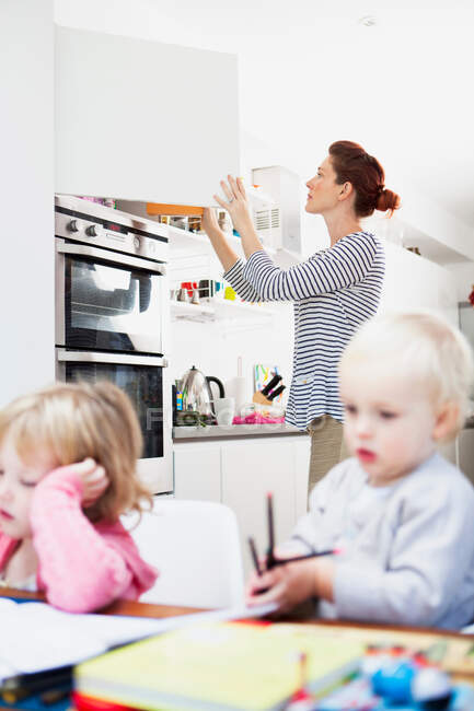 Mother opening kitchen cupboard — Stock Photo