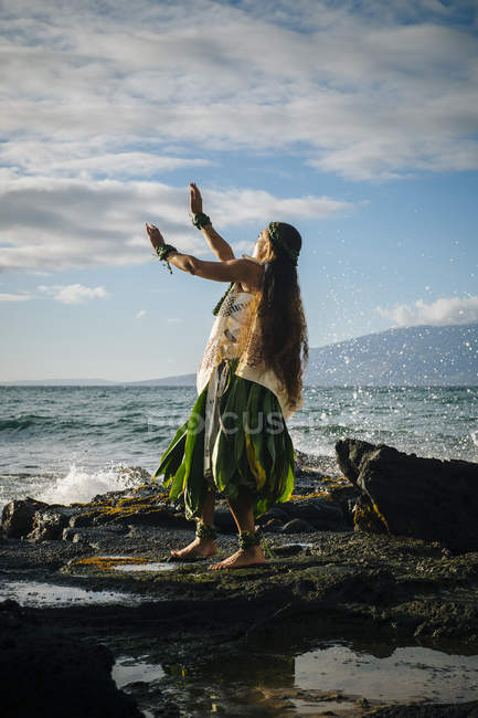 Mujer joven bailando hula en rocas costeras con traje tradicional, Maui, Hawaii, EE.UU. - foto de stock
