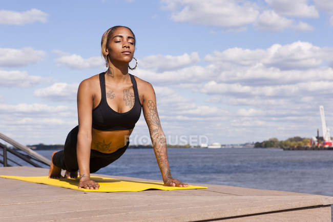 Junge Frau, die sich in Yogaposition auf Händen am Wasser ausruht, Augen geschlossen, Philadelphia, Pennsylvania, USA — Stockfoto