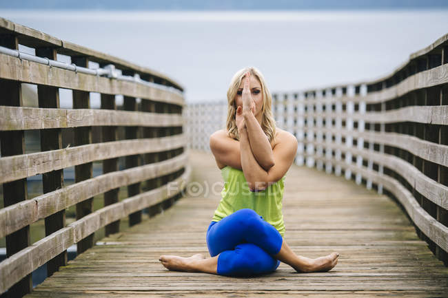 Portrait of young woman practicing yoga pose on wooden pier — Stock Photo